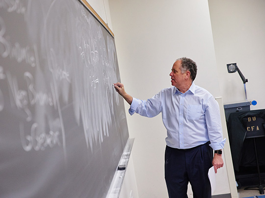 Associate Professor of the Practice Hal Tepfer writes equations on a chalkboard in an Actuarial Science classroom