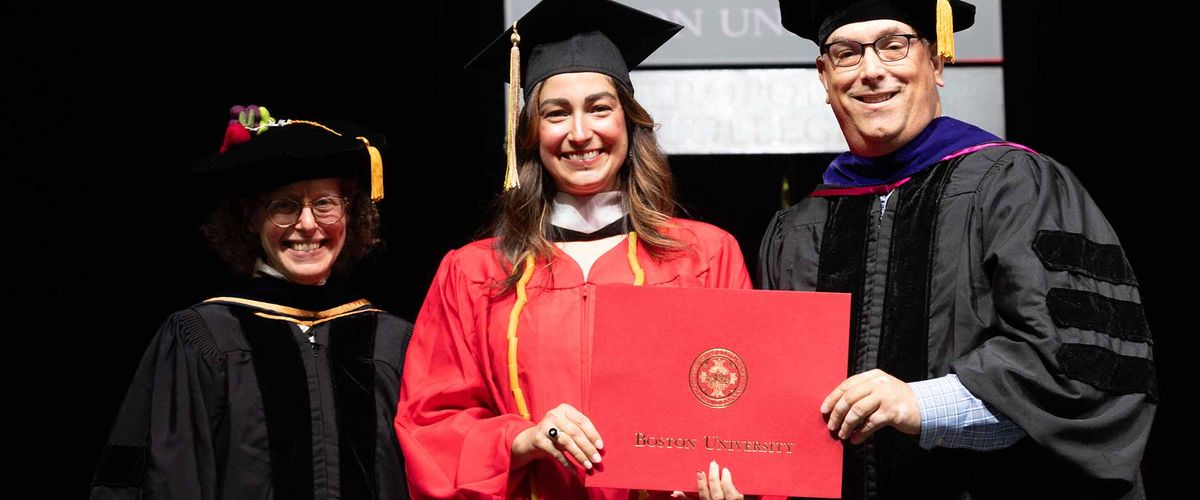 A student award winner poses with MET professors Shea Cronin and Megan Elias on stage during commencement