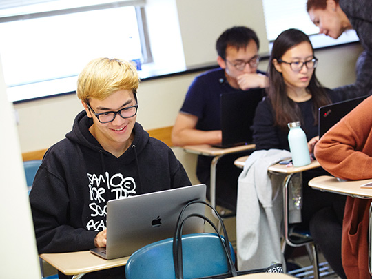 A BU MET student taking notes on a laptop in a classroom