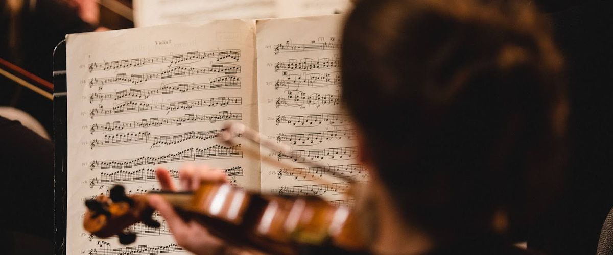 Looking over the shoulder of a woman playing the violin. The sheet music in front of her is in focus.