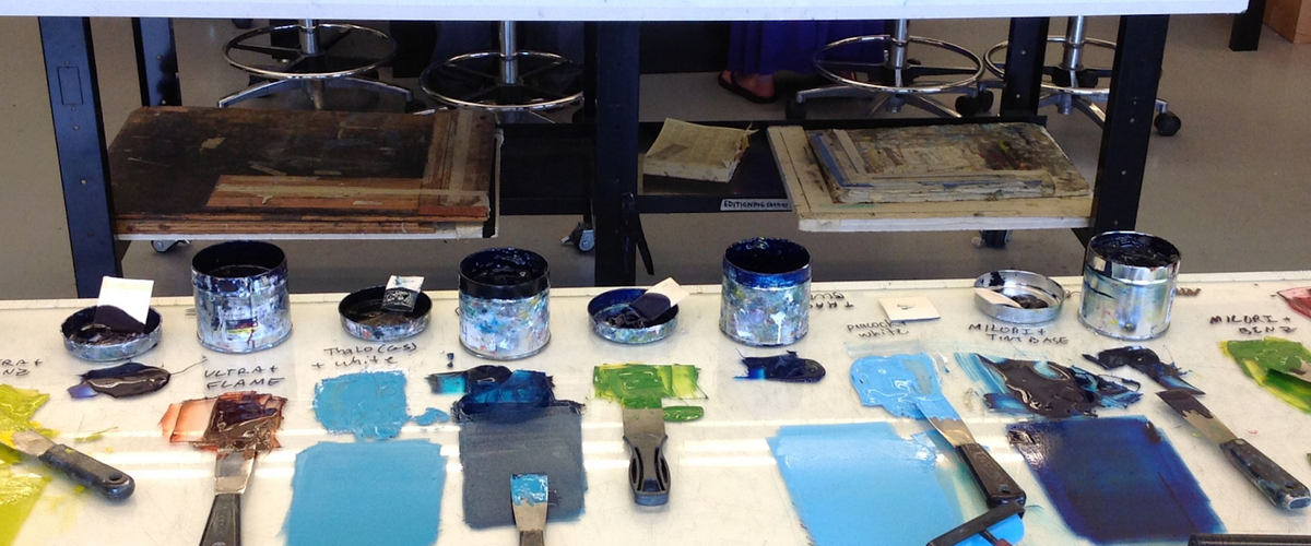 An assortment of different paints and paint brushes and rollers laid out on two tables