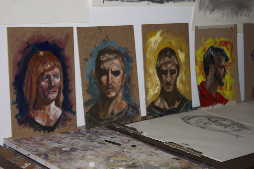 A series of portraits lined up along a table set against a wall.