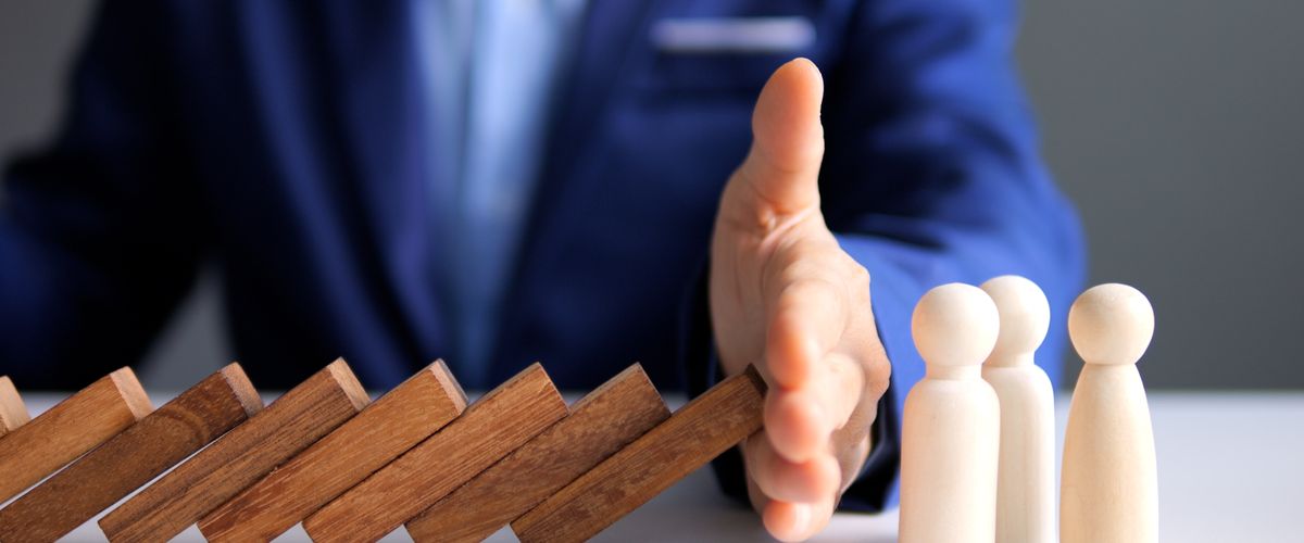 Closeup of a man's hand stopping a row of dominos from toppling into three wooden figures