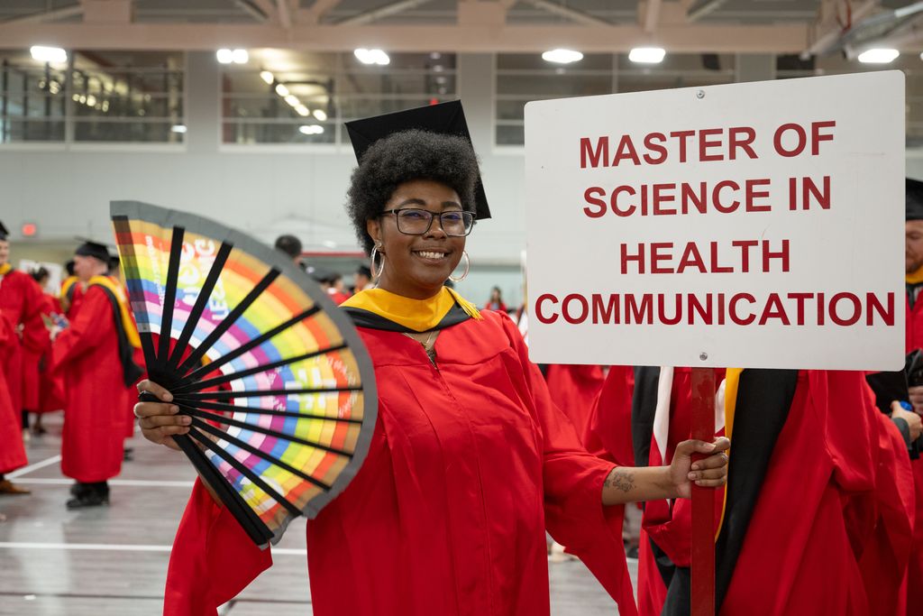 Woman in cap and gown holding rainbow fan and sign