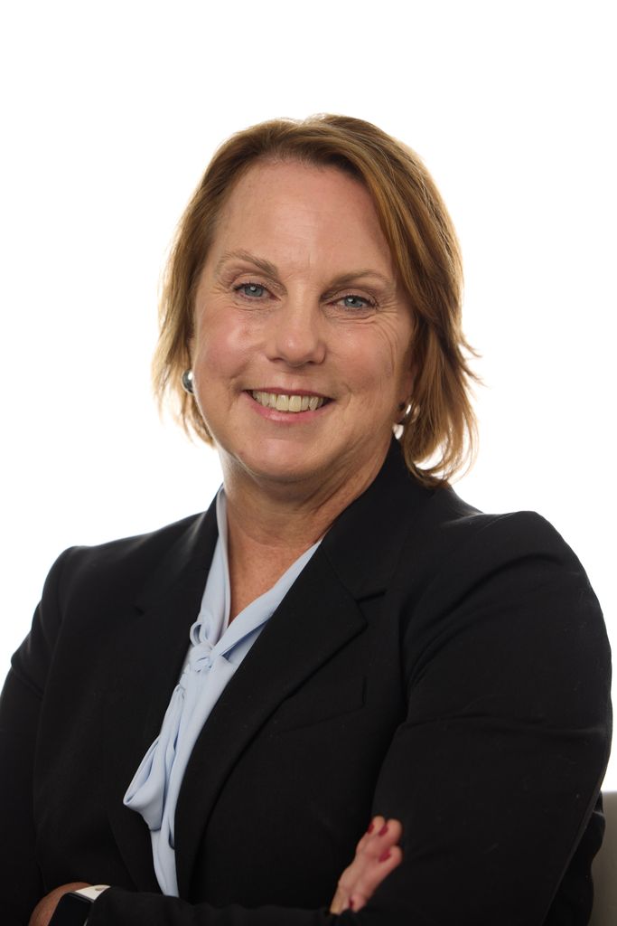 Headshot of a woman with blonde hair. She's smiling at the camera and wearing a black jacket with a light blue top.