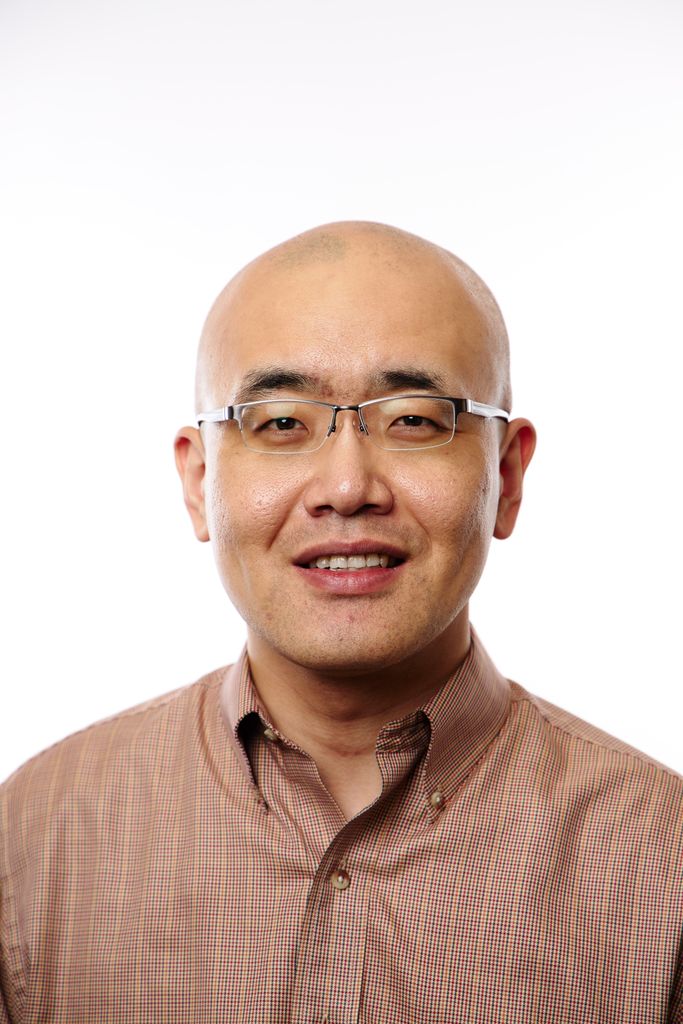 Headshot of a man with glasses. He's bald and smiling at the camera, and he's wearing a tan or orange buttonup with thin stripes.