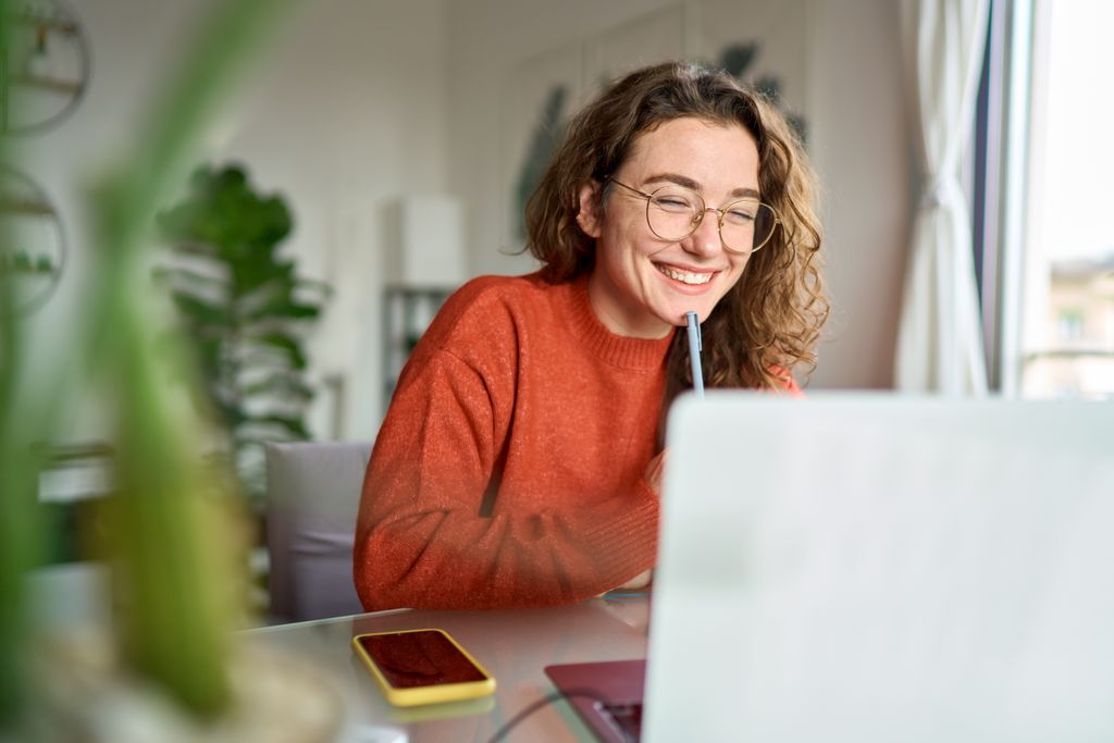 Woman in orange sweater smiling at open laptop