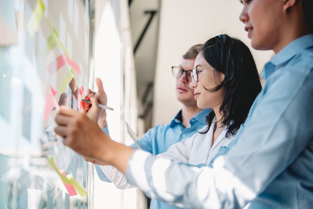 Three people writing and placing post-it notes on a glass window