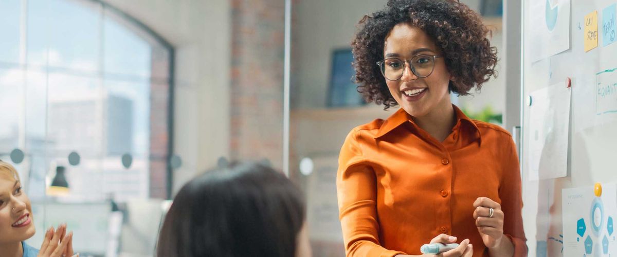 A business analyst presenting data on a whiteboard to a group in a conference room