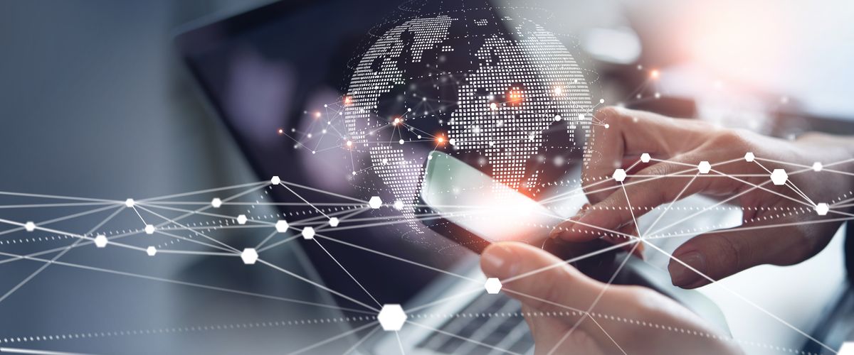 stock image of person holding a mobile device in front of a laptop with a globe behind it