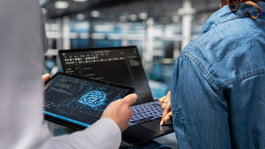 A person holding a tablet comparing data with a person using a laptop.