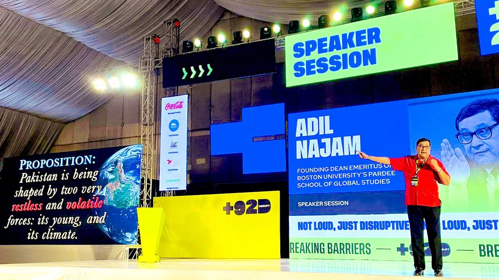 Adil Najam stands in front of multiple screens on stage at +92Disrupt in Karachi, Pakistan.