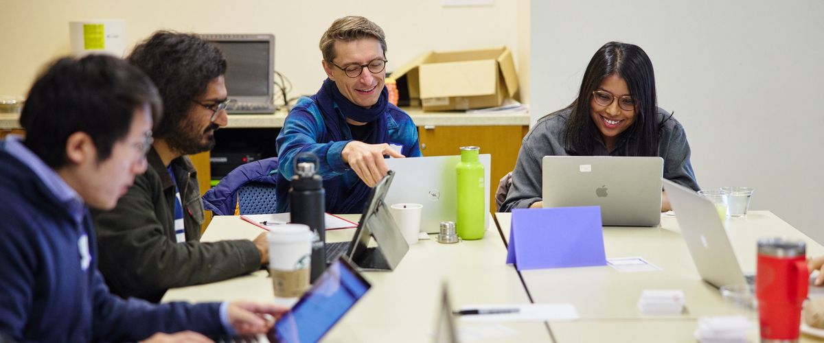 Smiling students chat as they work together on their laptops.