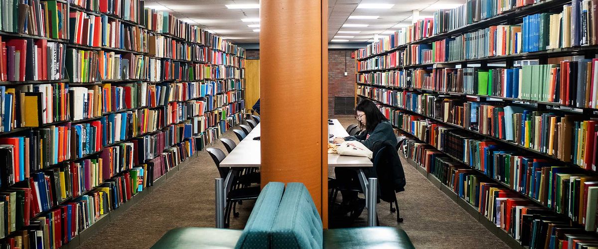 A lone student works between stacks of books in Mugar Library.