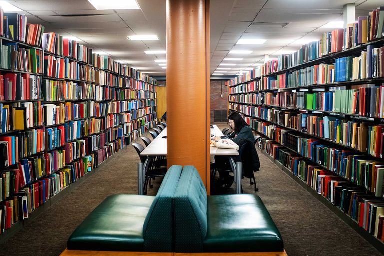 A lone student works between stacks of books in Mugar Library.