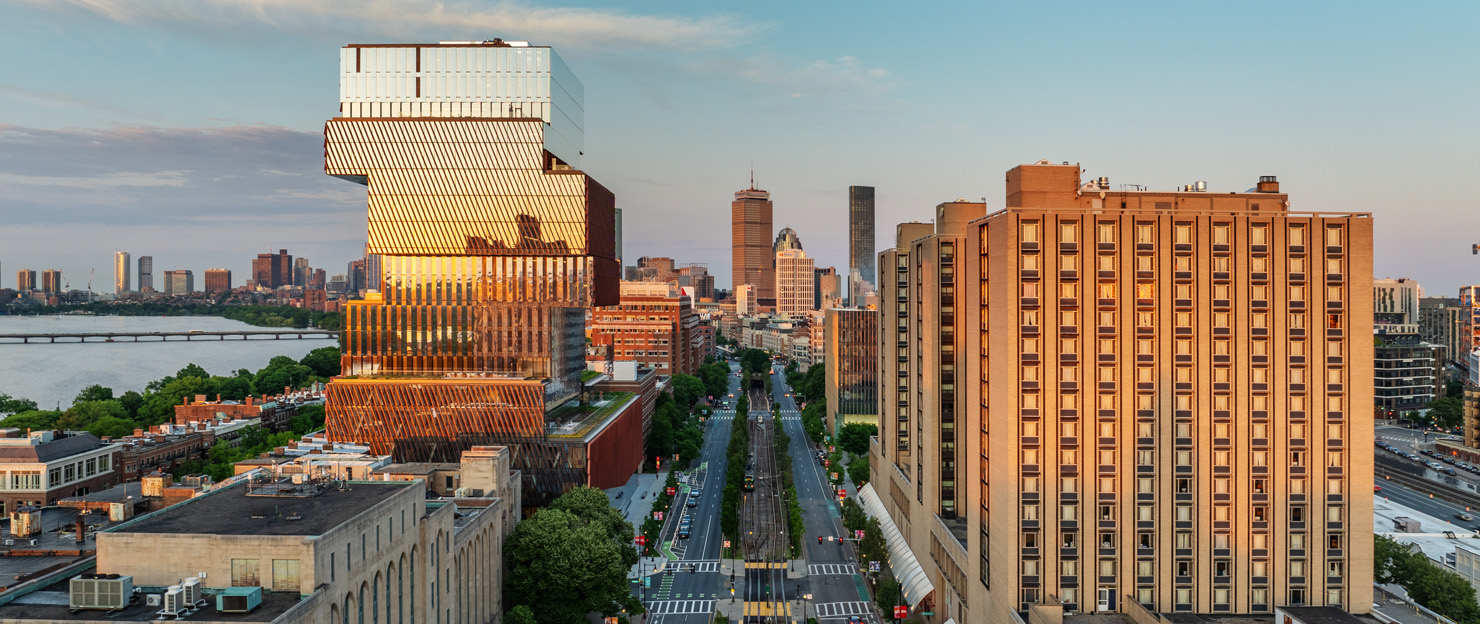 An aerial view of BU campus looking east at sunset. Commonwealth Ave stretches from the foreground toward the horizon, Warren Towers and the Center for Computing & Data Sciences are bathed in golden sunlight.
