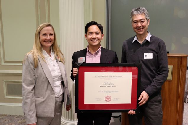 Three people hold an advising award against a formal ballroom wall