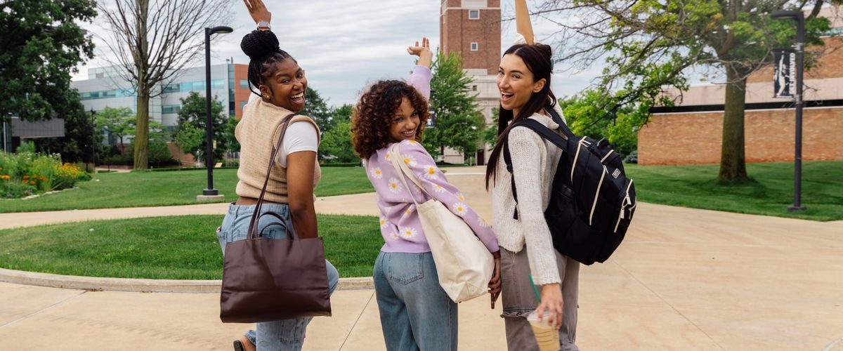 Three young adults with school bags turning their heads around to smile at the camera