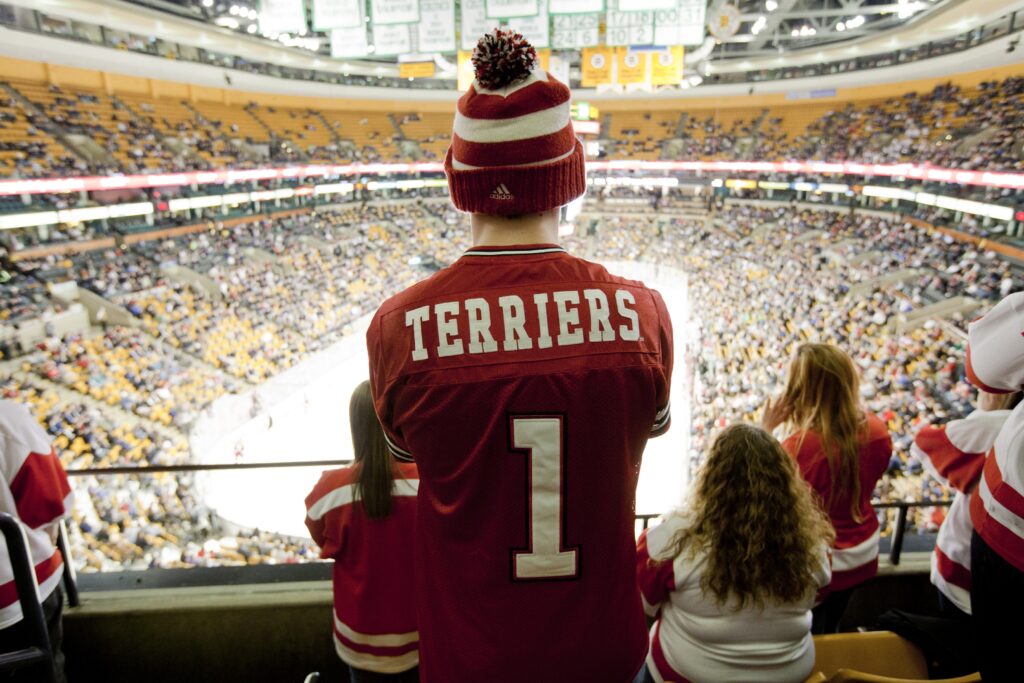 Person with a BU hockey jersey stands in the arena looking out at a the beanpot hockey game