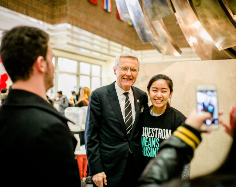 Allen Questrom and student smile for photo in atrium