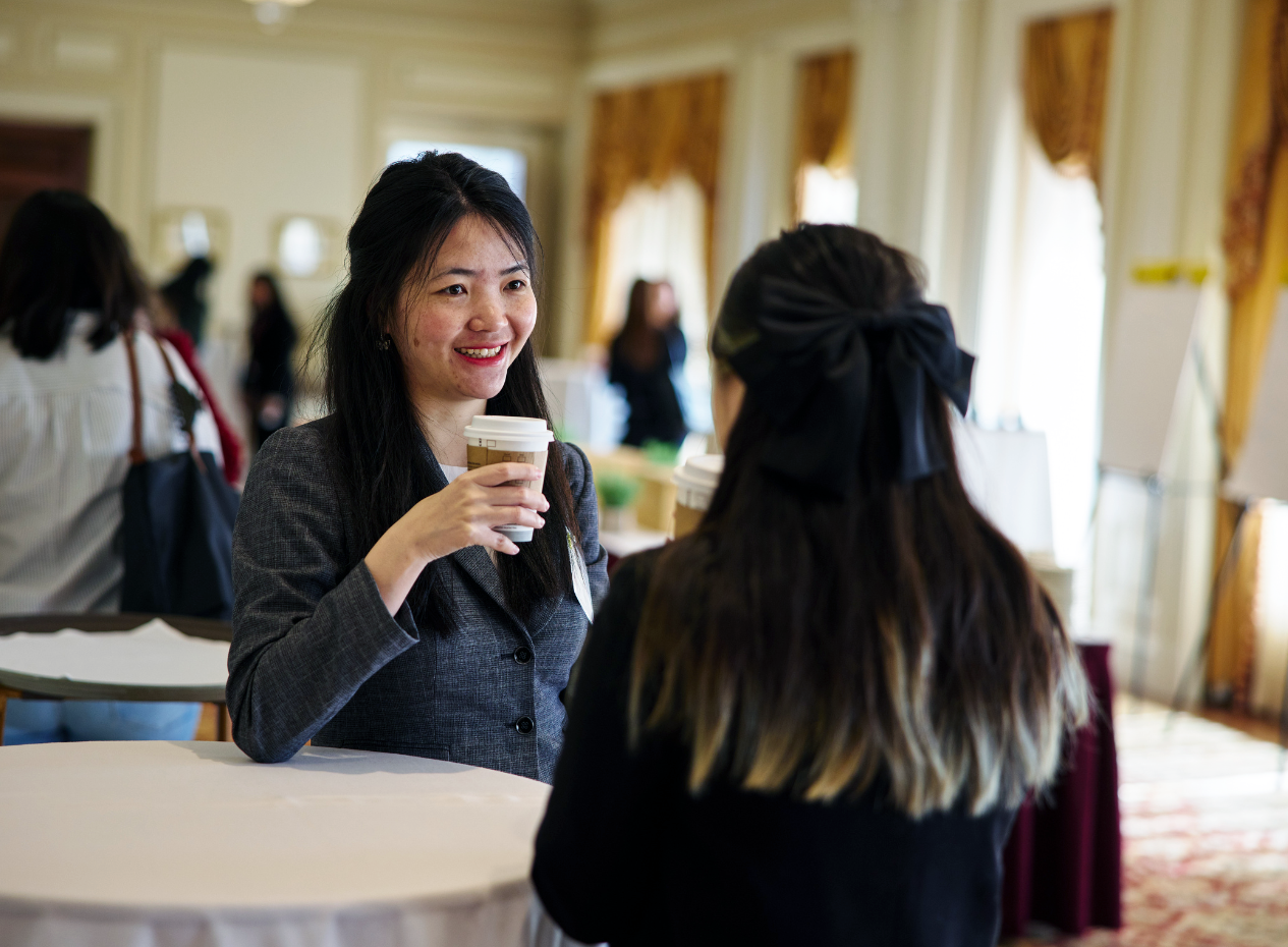Two women students stand at a round table and chat