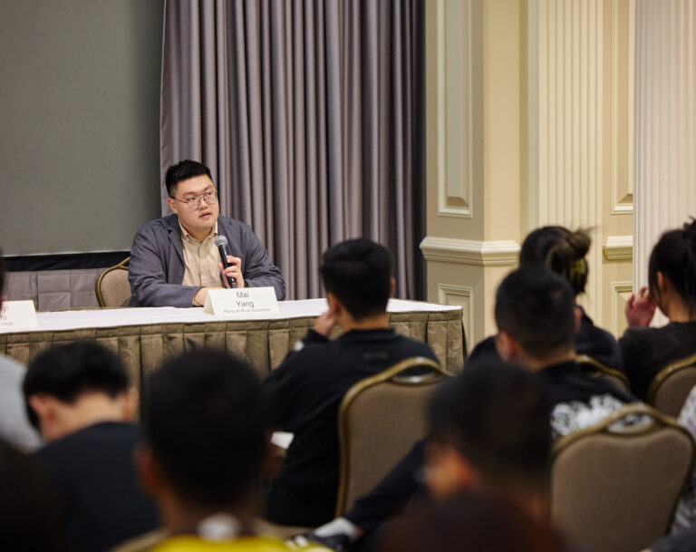 Student sitting in front of a microphone in front of a group of people.