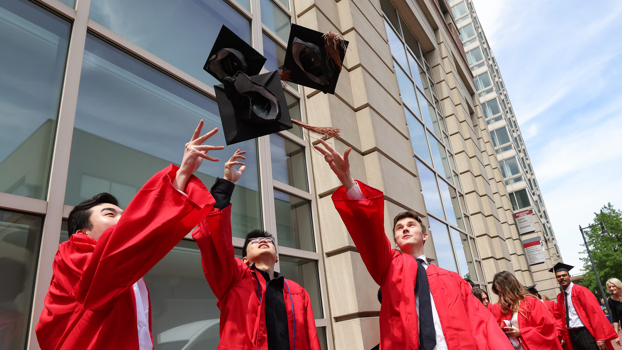 three grads in gowns throw caps into the air