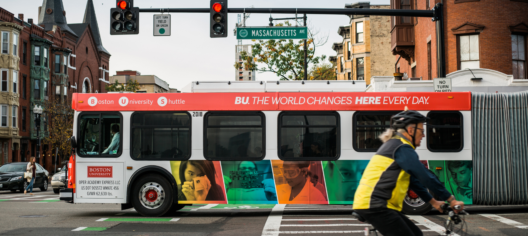 A Boston University bus drives across Massachusetts Ave. The side of the bus reads "BU. The world changes here every day."