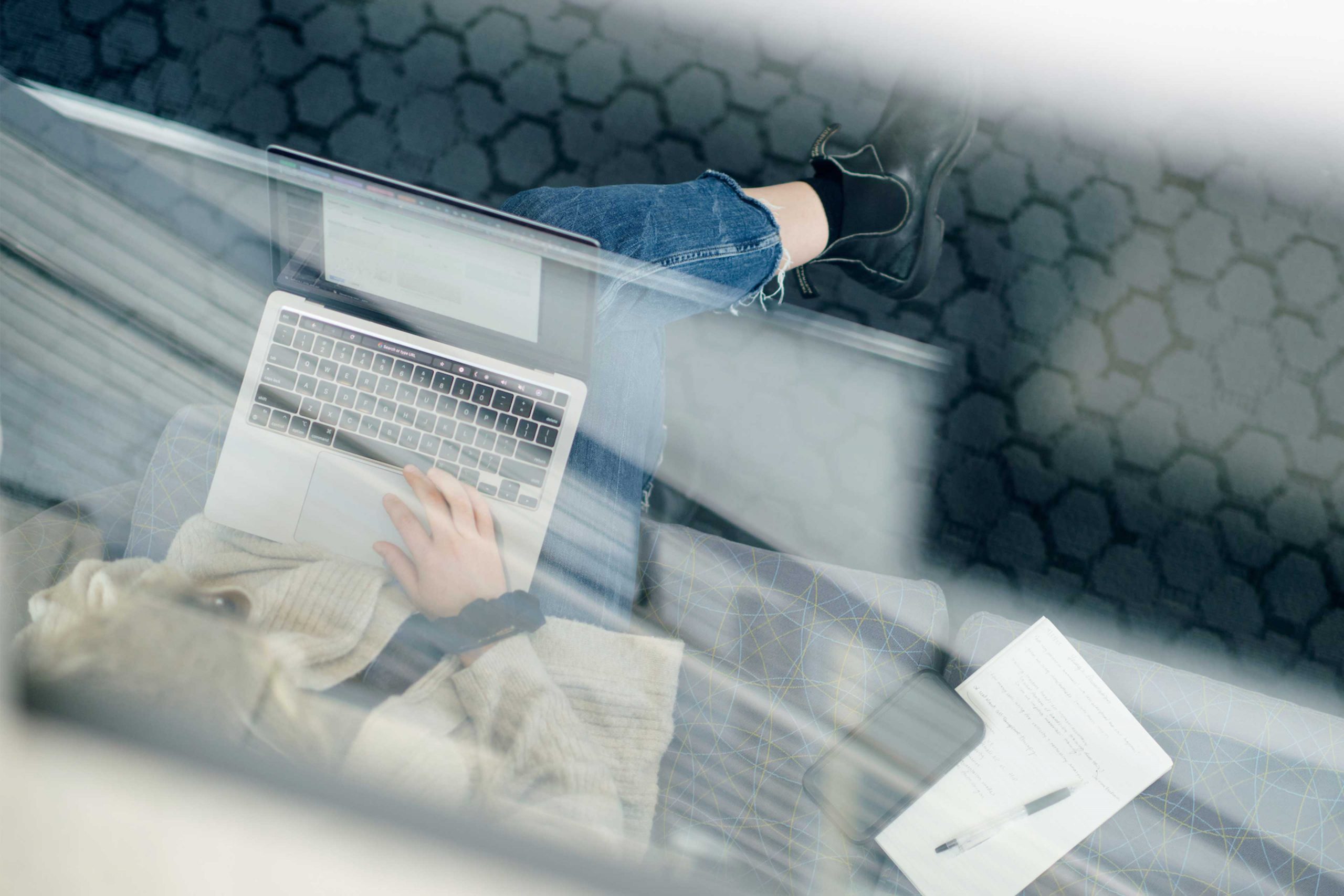 A view from above a person working on their laptop. They are sitting on a couch and have a black scrunchie on their wrist as they work on a grey and black laptop.