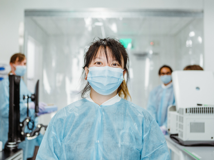 A person wearing a mask and a gown stands in a lab