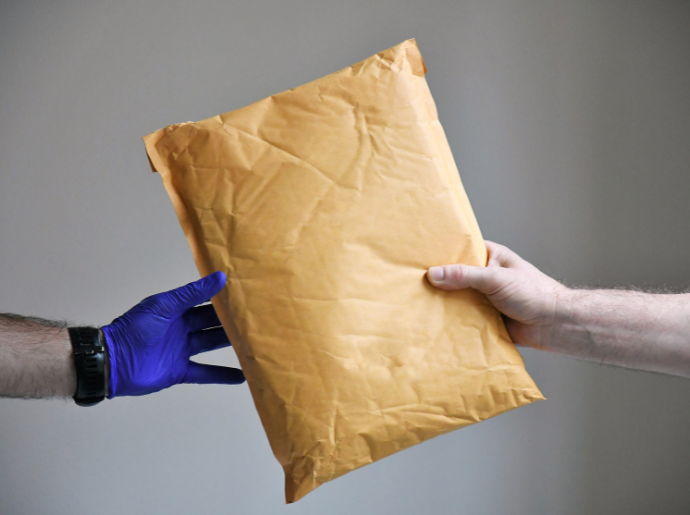 A person wearing a glove hands a person not wearing a glove a package.