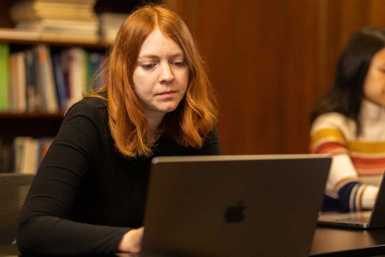 A person with shoulder length red hair sits at a computer