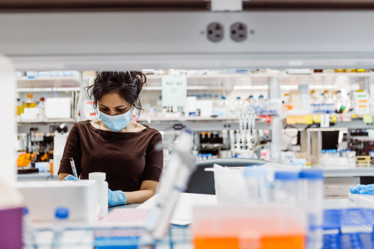 a person wearing gloves and mask works at a lab bench