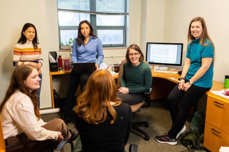 A group of people sit in a circle in an office smiling and talking.