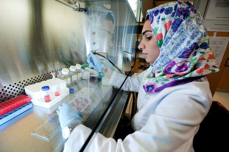 A person wearing gloves and a lab coat works in a hood on samples