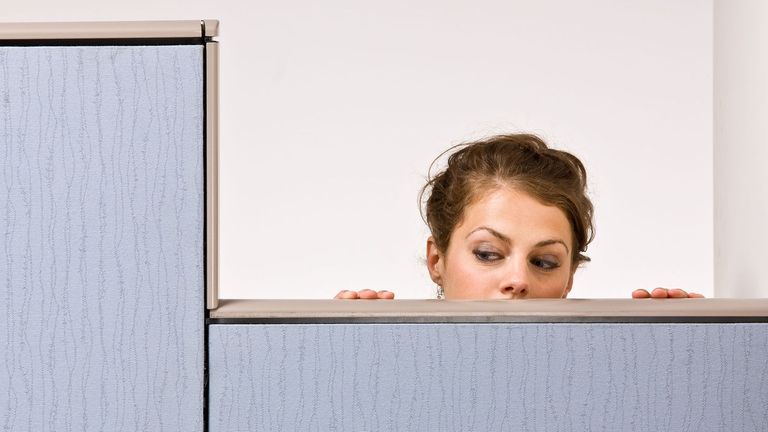 Nosy female coworker peering over cubicle wall