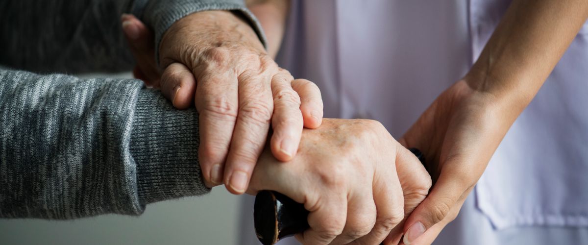 Close-up of hands of caretake and Parkinson's patient with a cane