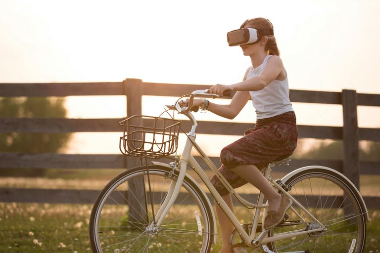 Girl wearing virtual reality goggles while riding a bike in front of a wooden fence
