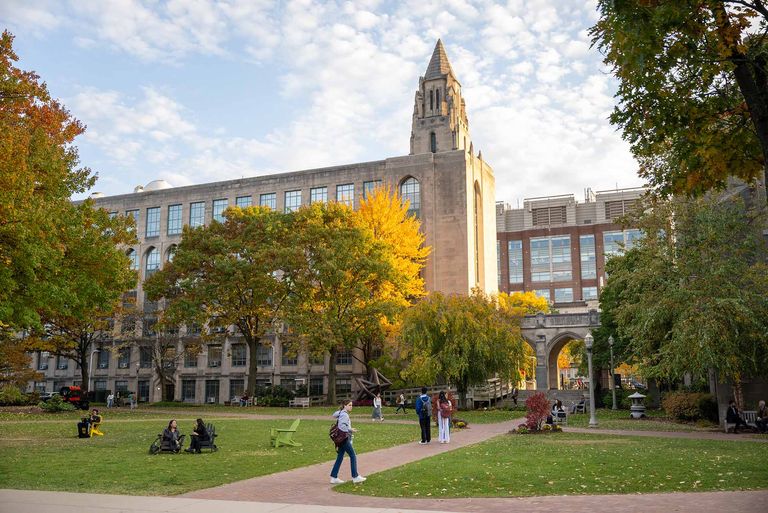 Various students walk across lawns and paths outside on BU's campus