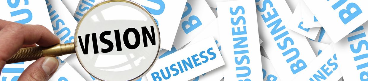 Hand holding up a magnifying glass to reveal the word "vision" over blue and white cards saying "business"
