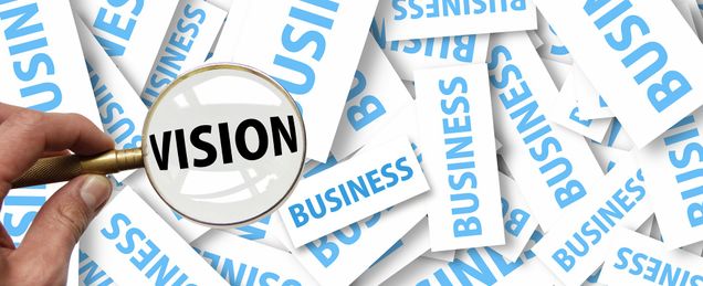 Hand holding up a magnifying glass to reveal the word "vision" over blue and white cards saying "business"