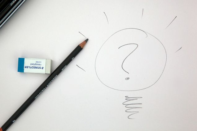 Black pencil on white paper next to eraser and a drawing of a light bulb with a question mark in it