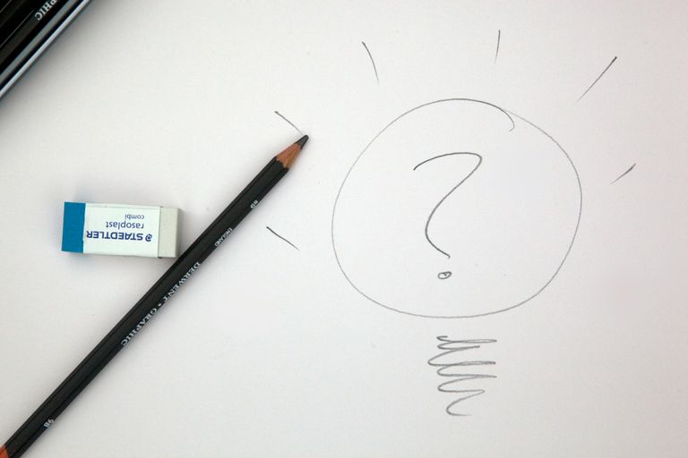 Black pencil on white paper next to eraser and a drawing of a light bulb with a question mark in it
