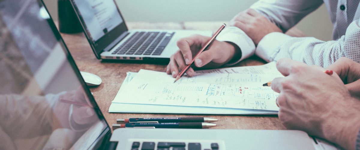 Hands of two people working on budget paperwork with two laptops on a wood desk