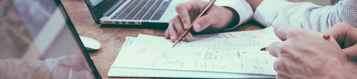 Hands of two people working on budget paperwork with two laptops on a wood desk