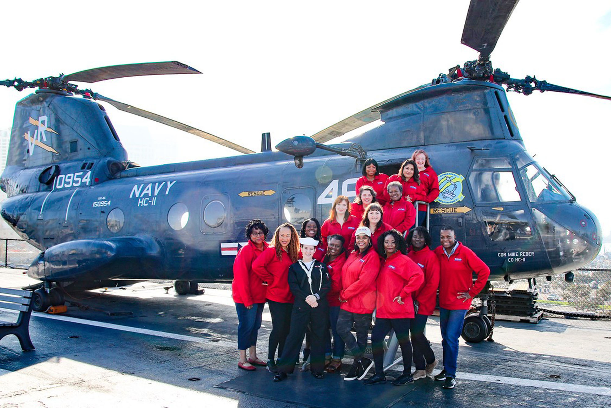 Group of women veterans in red jackets gathered in front of a US Navy helicopter