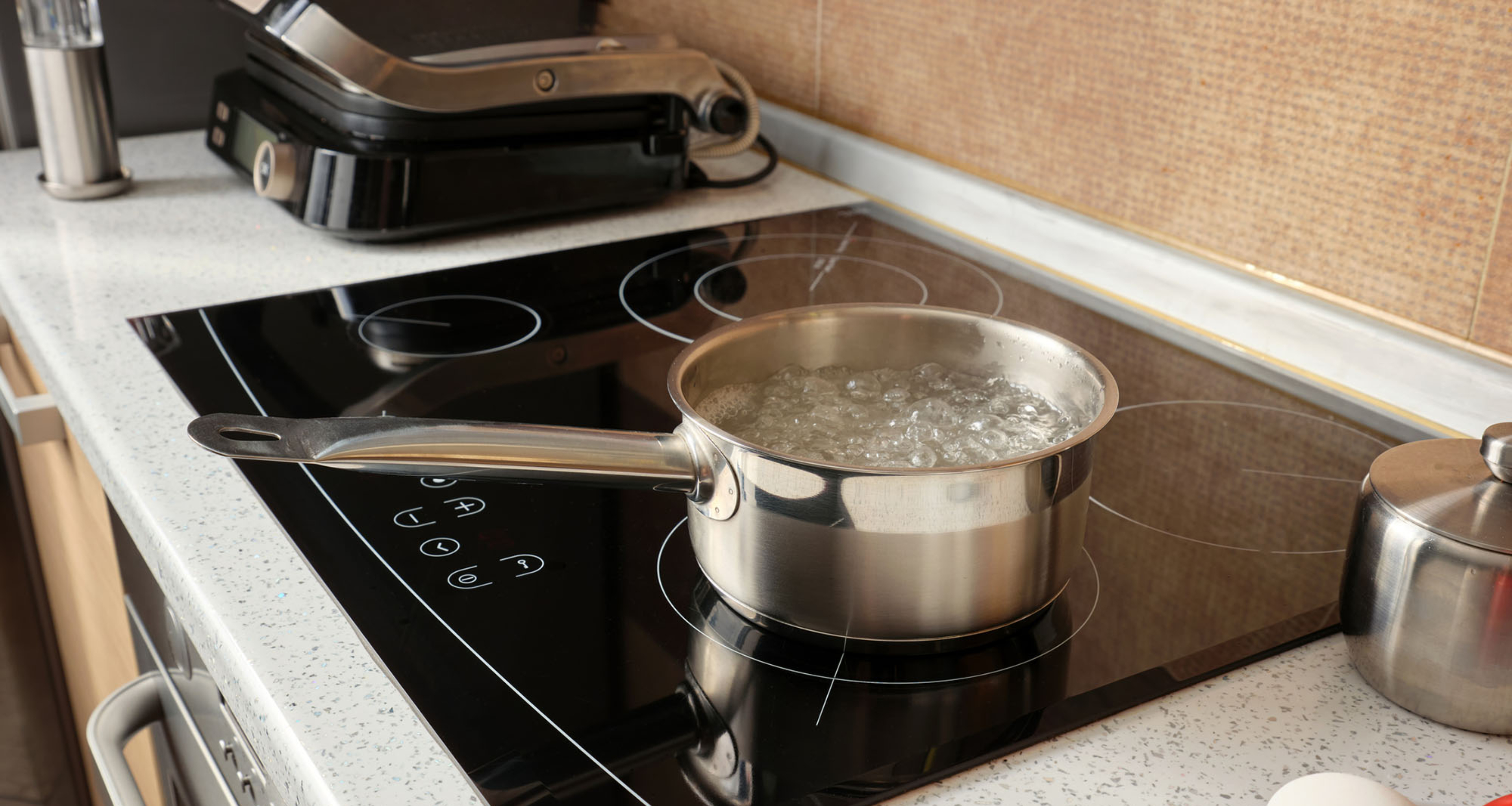Boiling water in a metal ladle on an induction cooker against the background of a kitchen.