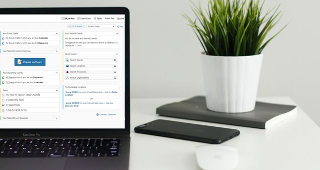 White table with open laptop showing the 25Live Homepage; a white mouse, a cell phone in a black cover, a black notebook with a small potted plant on top of it.