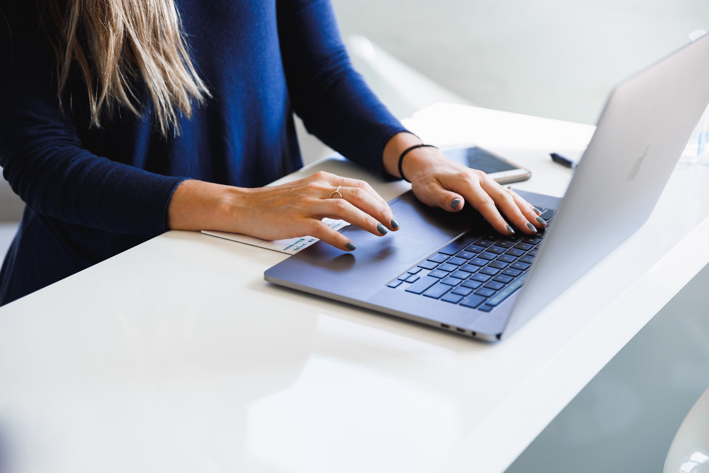 Hands of person wearing a long sleeve blue shirt on an open silver laptop computer.