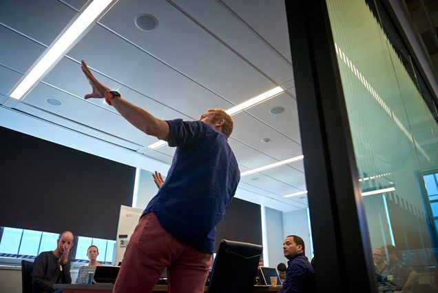 Rudolph Pienaar points at the front of the room, explaining a concept to developers seated around a conference table